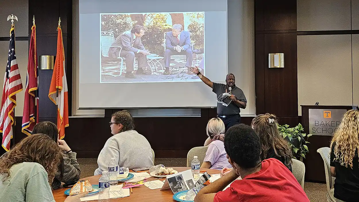 An image of an American civics presentation, a teacher at the head of the class gesturing toward an image projected onto a screen.